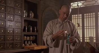 Movie still from “Iron Monkey” (1993), directed by Woo-Ping Yuen – A man holding a candle in a room with shelves; Medium shot, Low angle