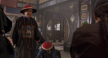 Movie still from “Iron Monkey” (1993), directed by Woo-Ping Yuen – An older man wearing a red hat in an oriental setting; Medium shot, Over the shoulder angle