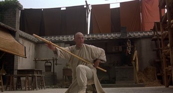 Movie still from “Iron Monkey” (1993), directed by Woo-Ping Yuen – A man holding a wooden stick while kneeling down; Wide shot, Low angle