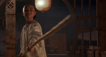 Movie still from “Iron Monkey” (1993), directed by Woo-Ping Yuen – A man holding a wooden stick in front of a lamp; Medium shot, Low angle
