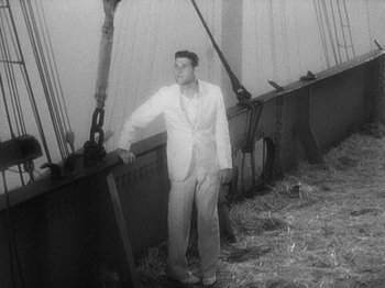 Movie still from “Island of Lost Souls” (1932), directed by Erle C. Kenton – A black and white photo of a man standing next to a boat; Wide shot, High angle