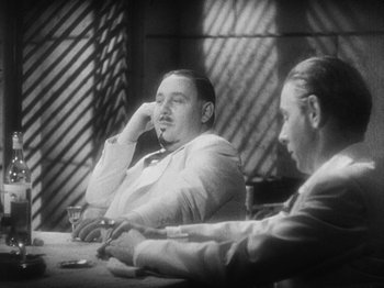 Movie still from “Island of Lost Souls” (1932), directed by Erle C. Kenton – Two men sitting at a table with a glass of whiskey; Medium shot, Low angle