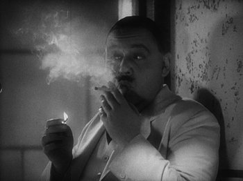 Movie still from “Island of Lost Souls” (1932), directed by Erle C. Kenton – A black and white photo of a man lighting a cigarette; Close Up shot, High angle