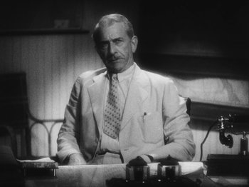 Movie still from “Island of Lost Souls” (1932), directed by Erle C. Kenton – An older man sitting at a desk in a suit and tie; Medium shot, Low angle