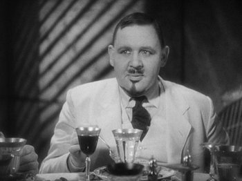 Movie still from “Island of Lost Souls” (1932), directed by Erle C. Kenton – A black and white photo of a man sitting at a table with a glass of red wine; Close Up shot, Over the shoulder angle