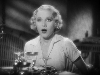 Movie still from “Island of Lost Souls” (1932), directed by Erle C. Kenton – A woman sitting at a table with a glass of wine; Close Up shot, Over the shoulder angle