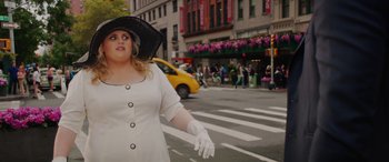 Movie still from “Isn't It Romantic” (2019), directed by Todd Strauss-Schulson – A woman in a white dress and black hat crossing the street; Medium shot, Over the shoulder angle