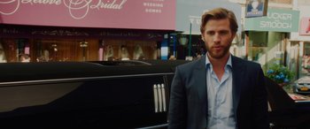 Movie still from “Isn't It Romantic” (2019), directed by Todd Strauss-Schulson – A man standing next to a car in front of a bridal store; Medium shot, Over the shoulder angle
