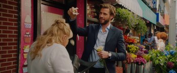 Movie still from “Isn't It Romantic” (2019), directed by Todd Strauss-Schulson – A man in a blue suit is handing a flower to a woman in a white dress; Medium shot, Over the shoulder angle