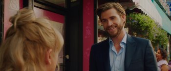 Movie still from “Isn't It Romantic” (2019), directed by Todd Strauss-Schulson – A man in a blue shirt and a suit smiling for the camera; Close Up shot, Over the shoulder angle