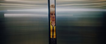 Movie still from “Isn't It Romantic” (2019), directed by Todd Strauss-Schulson – A woman with blonde hair and polka dot shirt peeking out of an elevator door; Medium shot, Overhead angle