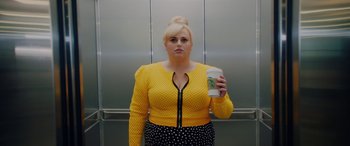 Movie still from “Isn't It Romantic” (2019), directed by Todd Strauss-Schulson – A woman holding a cup of coffee standing in front of an elevator; Medium shot, Over the shoulder angle