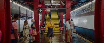 Movie still from “Isn't It Romantic” (2019), directed by Todd Strauss-Schulson – A group of people standing in front of a yellow escalator; Wide shot, Low angle