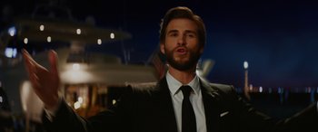 Movie still from “Isn't It Romantic” (2019), directed by Todd Strauss-Schulson – A man wearing a suit and tie standing in front of a building; Close Up shot, Low angle