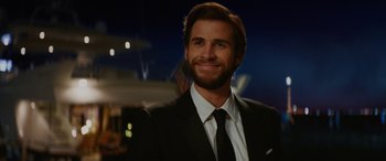 Movie still from “Isn't It Romantic” (2019), directed by Todd Strauss-Schulson – A man wearing a suit and tie smiling for the camera; Close Up shot, Over the shoulder angle