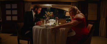 Movie still from “Isn't It Romantic” (2019), directed by Todd Strauss-Schulson – A man and a woman sitting at a dinner table; Medium shot, Over the shoulder angle