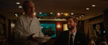 Movie still from “Isn't It Romantic” (2019), directed by Todd Strauss-Schulson – A man wearing a suit and tie holding a plate; Medium shot, Over the shoulder angle