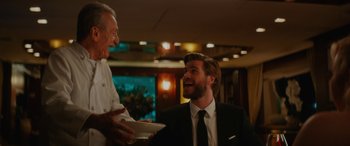 Movie still from “Isn't It Romantic” (2019), directed by Todd Strauss-Schulson – A man in a suit and tie talking to a man in a chef's outfit; Medium shot, Over the shoulder angle
