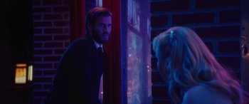 Movie still from “Isn't It Romantic” (2019), directed by Todd Strauss-Schulson – A man in a suit and tie standing in front of a window; Medium shot, Over the shoulder angle