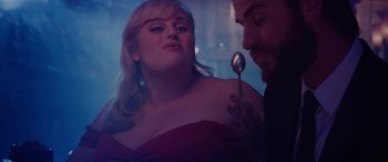 Movie still from “Isn't It Romantic” (2019), directed by Todd Strauss-Schulson – A woman in a red dress holding a spoon; Medium shot, Over the shoulder angle