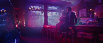 Movie still from “Isn't It Romantic” (2019), directed by Todd Strauss-Schulson – A man and a woman sitting on a bench in front of a projection screen; Wide shot, Low angle