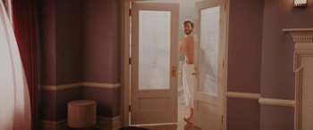 Movie still from “Isn't It Romantic” (2019), directed by Todd Strauss-Schulson – A man standing in a bathroom with a towel around his legs; Wide shot, Over the shoulder angle
