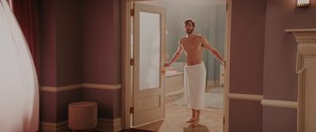 Movie still from “Isn't It Romantic” (2019), directed by Todd Strauss-Schulson – A man standing in a bathroom with a towel around his ankles; Wide shot, Over the shoulder angle