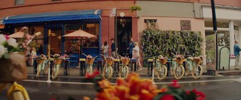 Movie still from “Isn't It Romantic” (2019), directed by Todd Strauss-Schulson – A group of people standing next to parked bicycles; Wide shot, Over the shoulder angle