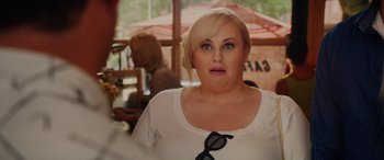 Movie still from “Isn't It Romantic” (2019), directed by Todd Strauss-Schulson – A woman with blonde hair wearing a white shirt and black glasses; Close Up shot, Over the shoulder angle