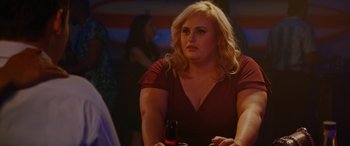 Movie still from “Isn't It Romantic” (2019), directed by Todd Strauss-Schulson – A woman sitting at a table holding a beer; Close Up shot, Over the shoulder angle