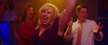 Movie still from “Isn't It Romantic” (2019), directed by Todd Strauss-Schulson – A woman with her mouth wide open is holding her arm up; Medium shot, Low angle