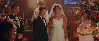 Movie still from “Isn't It Romantic” (2019), directed by Todd Strauss-Schulson – A man and a woman standing in front of a priest; Medium shot, High angle