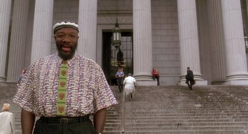Movie still from “It Could Happen to You” (1994), directed by Andrew Bergman – A man standing in front of a building on some steps; Medium shot, Low angle