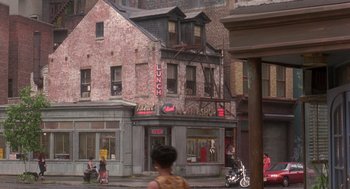 Movie still from “It Could Happen to You” (1994), directed by Andrew Bergman – A woman standing on the sidewalk in front of a building; Extreme Wide shot, High angle
