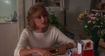 Movie still from “It Could Happen to You” (1994), directed by Andrew Bergman – A woman sitting at a table with a hot dog in front of her; Close Up shot, Over the shoulder angle