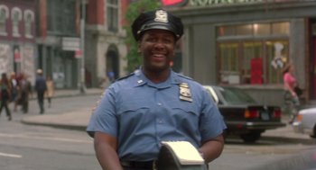 Movie still from “It Could Happen to You” (1994), directed by Andrew Bergman – A man in a police uniform smiles for the camera; Medium shot, Low angle