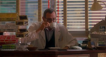 Movie still from “It Could Happen to You” (1994), directed by Andrew Bergman – A man sitting at a table drinking a cup of coffee; Medium shot, Over the shoulder angle