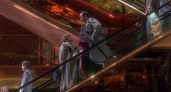 Movie still from “It Could Happen to You” (1994), directed by Andrew Bergman – A man and a woman on an escalator with luggage; Wide shot, Low angle