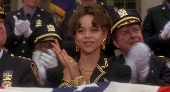 Movie still from “It Could Happen to You” (1994), directed by Andrew Bergman – A woman wearing a suit and gold jewelry clapping; Close Up shot, Over the shoulder angle
