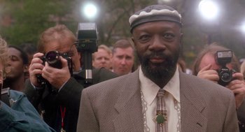 Movie still from “It Could Happen to You” (1994), directed by Andrew Bergman – A man in a suit and a hat standing in front of a camera; Close Up shot, Low angle