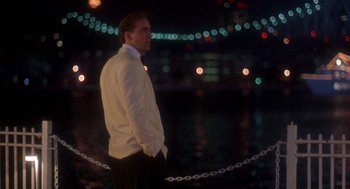 Movie still from “It Could Happen to You” (1994), directed by Andrew Bergman – A man in a white jacket standing in front of a body of water at night; Medium shot, Over the shoulder angle