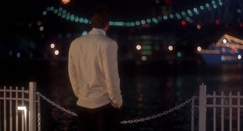 Movie still from “It Could Happen to You” (1994), directed by Andrew Bergman – A man standing in front of a city at night; Medium shot, Over the shoulder angle