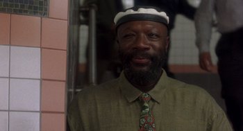 Movie still from “It Could Happen to You” (1994), directed by Andrew Bergman – A man wearing a hat and a tie smiling for the camera; Close Up shot, Low angle