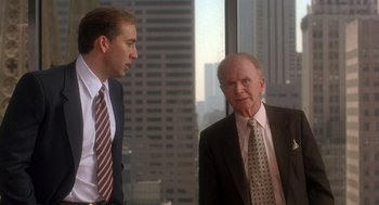 Movie still from “It Could Happen to You” (1994), directed by Andrew Bergman – Two men in business suits talking in front of a window; Medium shot, Over the shoulder angle