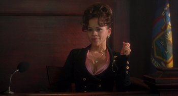 Movie still from “It Could Happen to You” (1994), directed by Andrew Bergman – A woman sitting at a table in front of a wooden wall; Medium shot, High angle