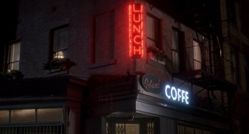 Movie still from “It Could Happen to You” (1994), directed by Andrew Bergman – A neon sign on the side of a building; Wide shot, Low angle