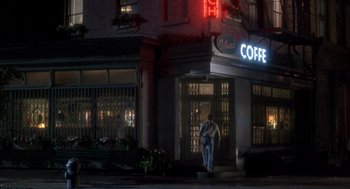 Movie still from “It Could Happen to You” (1994), directed by Andrew Bergman – A man walking in front of a coffee shop at night; Wide shot, Over the shoulder angle
