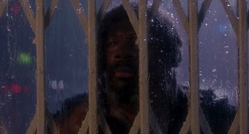 Movie still from “It Could Happen to You” (1994), directed by Andrew Bergman – A man looking out a window through a metal grate; Medium shot, Low angle