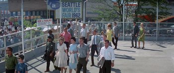 Movie still from “It Happened at the World's Fair” (1963), directed by Norman Taurog – A group of people walking down a sidewalk near a building; Wide shot, High angle