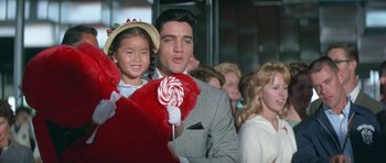 Movie still from “It Happened at the World's Fair” (1963), directed by Norman Taurog – A man and a little girl holding lollipops in a crowd; Medium shot, Over the shoulder angle